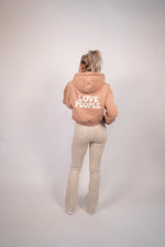Person wearing a beige hoodie with 'LOVE PEOPLE' text on the back, standing against a plain background