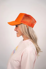Woman wearing an orange cap and light pink sweatshirt with a colorful design on a plain background