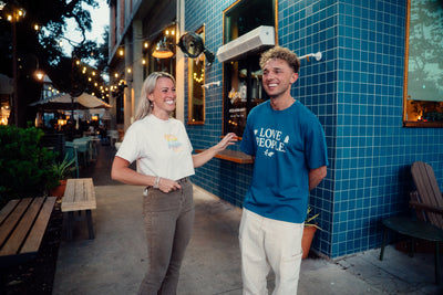 Two people standing outside a building with blue tiled walls. Love People clothing is being worn. Love People. Love People Apparel