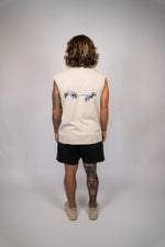 Person wearing a sleeveless beige shirt with a graphic design on the back, standing against a plain background.