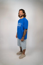 Man wearing a blue t-shirt with text and graphics on a plain background