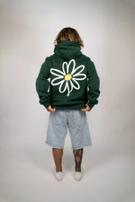 Person wearing a green hoodie with a white daisy design on the back against a plain background