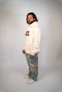 Person wearing a white hoodie with text and patterned pants on a plain background