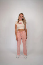 Woman wearing a beige t-shirt with text and pink pants on a white background