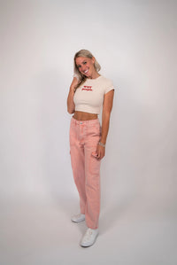 Woman wearing a beige crop top and pink jeans on a white background