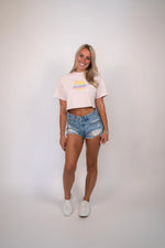 Woman wearing a white crop top and denim shorts on a plain background