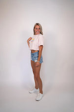 Woman wearing a pink crop top and denim shorts on a plain background