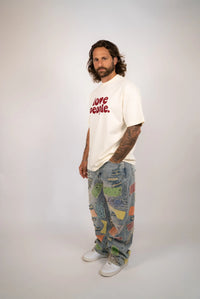 Person wearing a white t-shirt with text and colorful pants on a plain background
