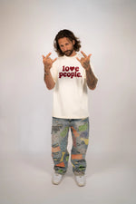 Person wearing a white t-shirt with 'love people' text and colorful pants on a plain background