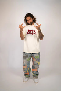 Person wearing a white t-shirt with 'love people' text and colorful pants on a plain background